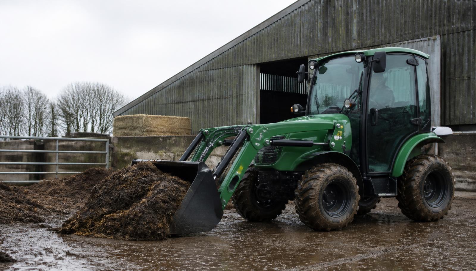 Generic electric tractor loading muck with a front loader in a farmyard